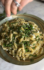 sprinkling herbs on dilly pasta salad made with not just co. dilly ranch dressing